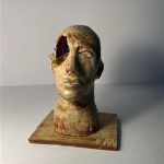 Gold colored head sculpture with a hole in the side of it